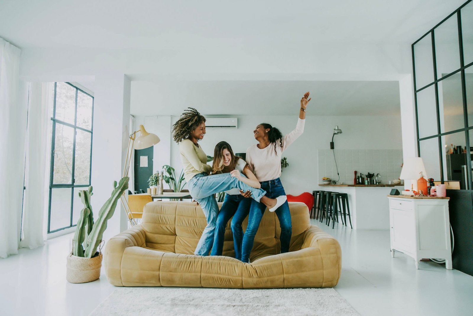Diverse group of female friends enjoying party and laughing together - Women friends having fun at home dancing on the couch - Happy lifestyle and friendship concept
