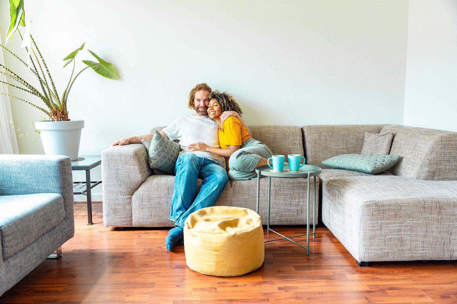 Cheerful multiracial couple sitting on sofa in the living room - Happy family moving in new home - Real estate and stylish furniture concept